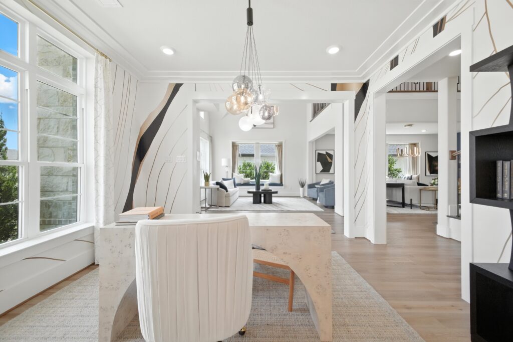Bright home office with large windows, a modern white desk, abstract wall art, and open sightlines into the living and dining areas of a contemporary home.