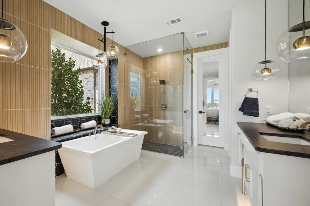 Modern bathroom with a freestanding white tub, glass walk-in shower, black and wood tile accents, double vanity with black countertops, and pendant lighting.