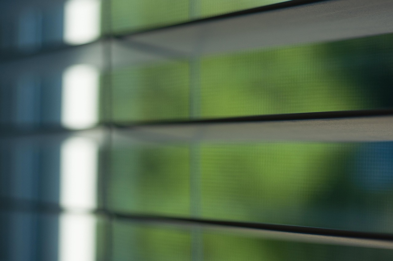 Close-up of horizontal mini blinds with natural light and greenery outside the window